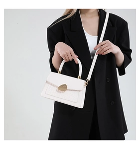 Détail du sac à main blanc à motif crocodile avec fermoir doré sur une tenue noire