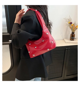 Chic red leather crescent bag with silver studs worn as a stylish underarm shoulder bag