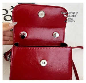 Detail of silver magnetic buckle closure on a red glossy leather crossbody handbag
