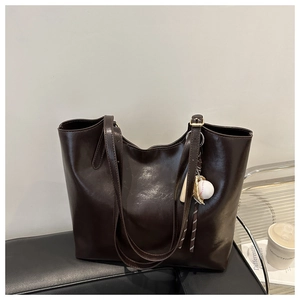Detail of dark brown leather tote bag with unique baseball and bat decorative pendant