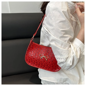 Détail du sac sous l'aisselle rouge embossé avec nœud doré et texture brillante