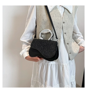 Detail of a black sequined handbag with a sculptural silver metal handle on a model