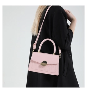 Sac à main rose effet crocodile porté par un mannequin en manteau noir élégant