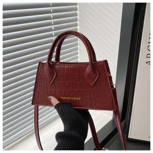 Detailed view of burgundy crocodile pattern leather bag with gold fashion lettering