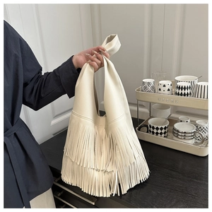 Dettaglio del design a tre strati di nappe su una borsa tote color crema in ecopelle