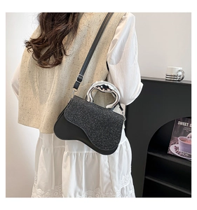 Detail shot of a black sequined crossbody bag with a curved design and silver handle