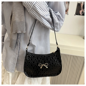 Detail of black textured underarm bag with a golden metal bow and glossy embossed finish