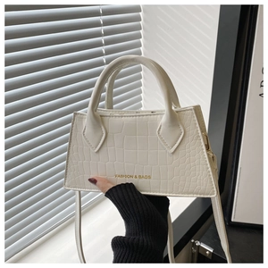Detail of white crocodile pattern handbag with gold fashion lettering and top handle