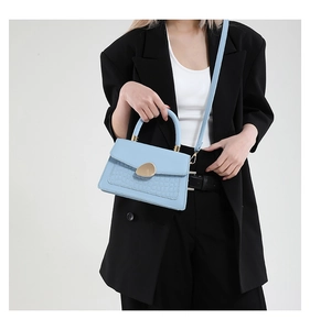 Sac bandoulière bleu à motif crocodile et boucle dorée porté par un mannequin