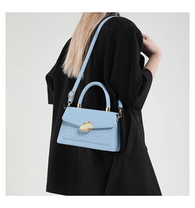 Détail du sac bandoulière bleu clair avec motif crocodile et boucle dorée sur manteau noir