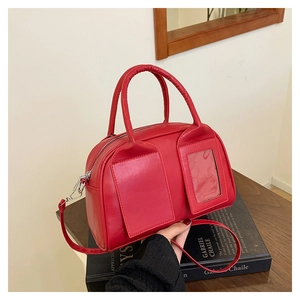 Detail of red Boston handbag featuring a transparent photo slot and double handles on books