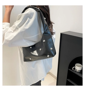 Close-up of black patent leather shoulder bag featuring oversized silver stud accents