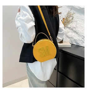 Macro detail of the yellow round handbag showing the gold SM metal logo and leather texture