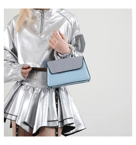 Detail of light blue color block handbag with metallic ring handle and grey textured flap