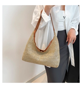 Detail of woven straw tote bag with brown leather shoulder strap shown on a model