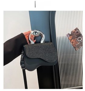 Detail of elegant black saddle bag with fluid silver metal handle and crystal flap