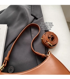 Detail of a brown leather shoulder bag with gold hardware and adjustable long strap