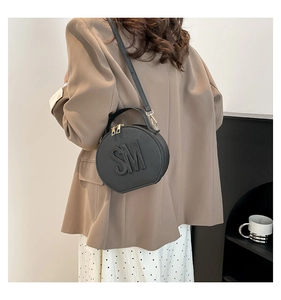 Detailed view of black round crossbody bag with SM embossed logo on a female model