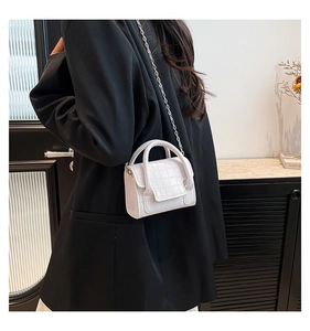 Gros plan du mini sac à bandoulière blanc gaufré croco avec chaîne sur un blazer noir