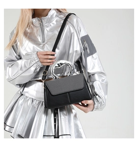 Detail of black crossbody bag with silver metal handle and woven flap texture on a model