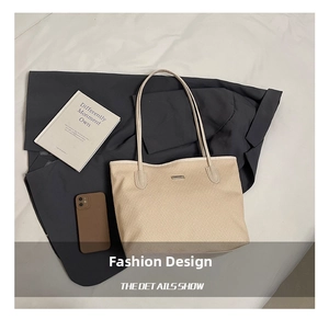 Detailed view of beige woven tote bag texture with slim leather straps and metal plate