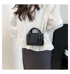 Detail of a black crocodile-embossed mini square bag with silver chain strap worn by a model
