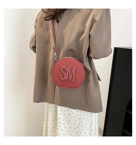 Detail of red circular handbag with embossed SM logo, styled with a brown blazer suit
