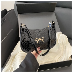 Detail of black patent leather bag with embossed texture and gold bow ornament