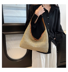 Detail of a large beige straw shoulder bag with brown leather trim and curved design