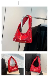 Detail view of red patent leather shoulder bag with silver studs and wide strap