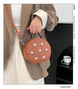 Détail du sac bandoulière rond marron à clous porté par un mannequin en blazer marron