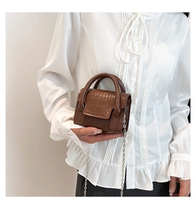 Detail of dark brown faux crocodile texture handbag with gold metal chain on a white blouse