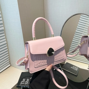 Sac à main rose en similicuir avec texture crocodile et fermoir doré devant miroir