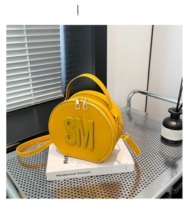 Detail of yellow round handbag with gold zippers and SM letter charm on a textured surface