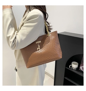 Close-up of brown woven texture tote bag featuring a gold chain and deer pendant charm