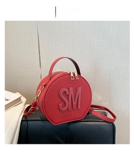 Detailed view of red circular cross-grain leather bag with embossed SM logo and gold hardware