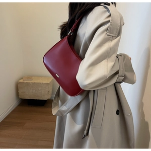 Close-up of stylish burgundy leather hobo bag worn with a beige trench coat
