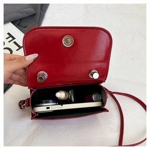 Detail of red glossy square bag interior holding a smartphone, lipstick and skincare