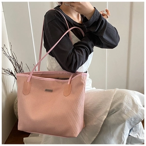 Pink woven tote bag with slim shoulder straps and metal logo detail shown on model