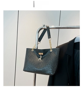 Detail of black woven tote bag featuring gold chain strap and deer charm on hanger