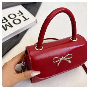 Detail of red glossy square handbag with silver metal bow and textured top handle