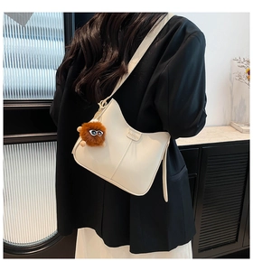 Détail du sac seau en cuir blanc cassé avec logo FASHION et breloque monstre en peluche