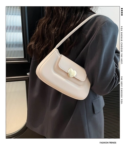 Detail of a chic cream underarm bag with a gold heart-shaped metal buckle on a grey suit