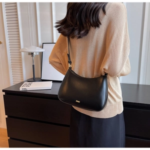 Detailed view of black matte leather baguette bag worn by model in minimalist studio