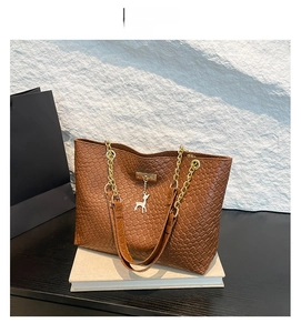 Detail of brown woven tote bag with gold chain strap and deer charm on white books