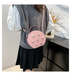 Pink round crossbody bag with silver studs shown on a model for size perspective