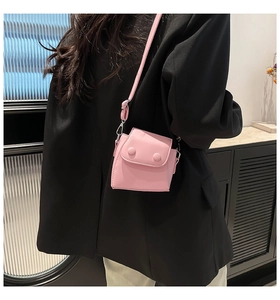 Pink mini crossbody bag featuring double round button design and slim strap on black blazer