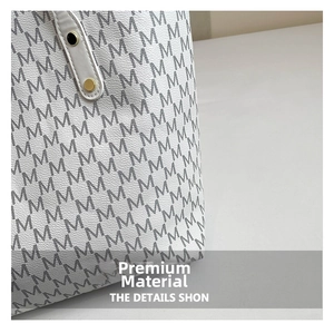 Detail of white tote bag with all-over M-letter print and golden rivet stitching