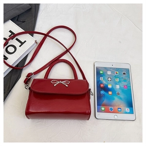 Red glossy patent leather handbag with silver bow detail next to a tablet for scale