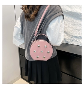 Détail d'un sac rond rose à clous argentés porté par un mannequin dans un cadre décontracté
